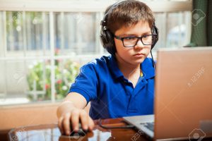 Portrait of a young boy with glasses playing some video games on a laptop computer